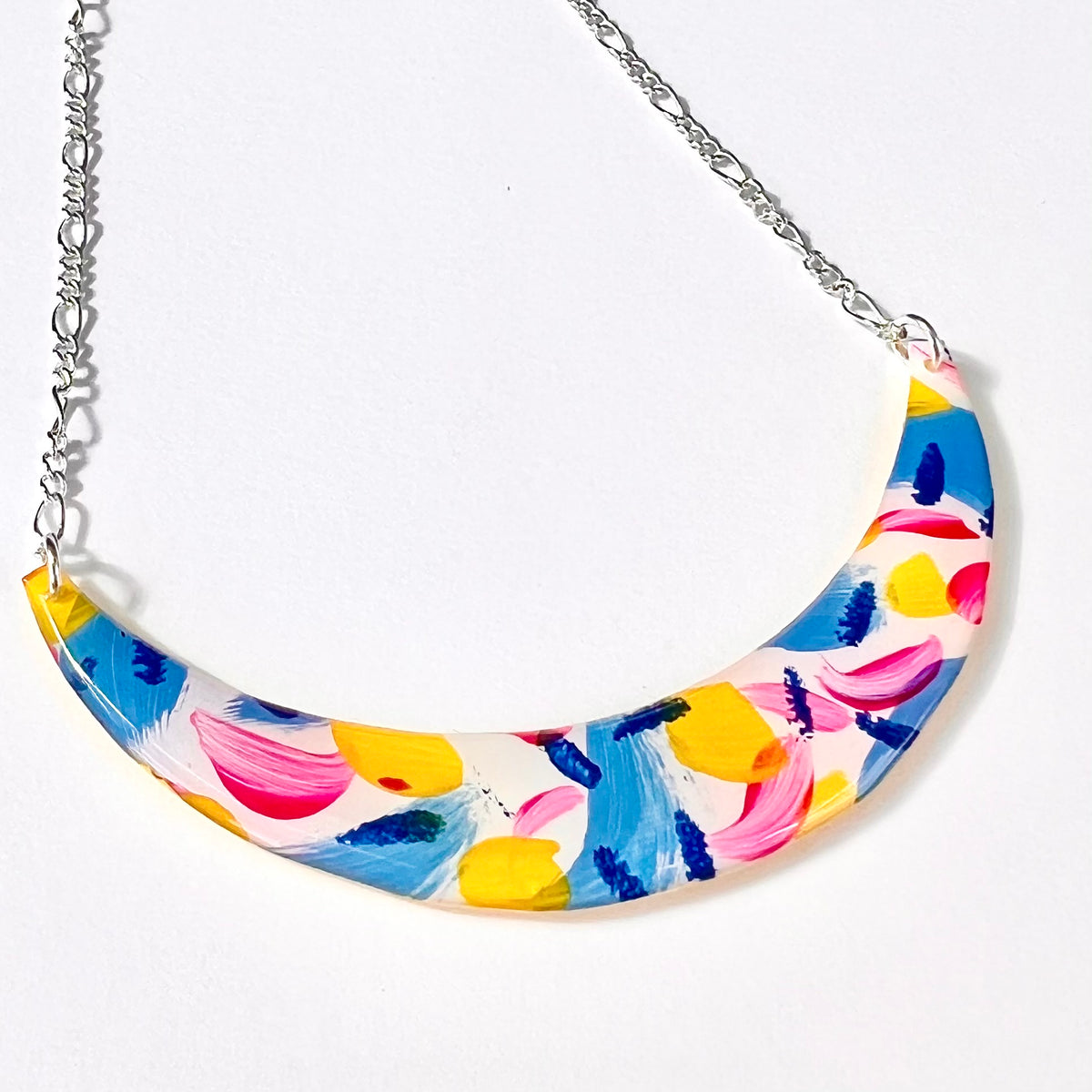 Close-up of colourful blue yellow and pink resin coated crescent pendant