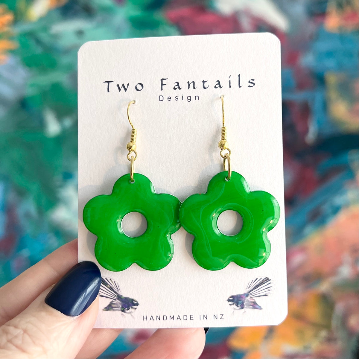 Bright glossy green five petal flower dangle earrings with circular cutouts and gold-tone hooks on Two Fantails Design display card