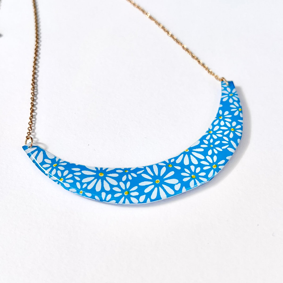 Close-up of hand-painted white daisies on blue resin-coated crescent pendant