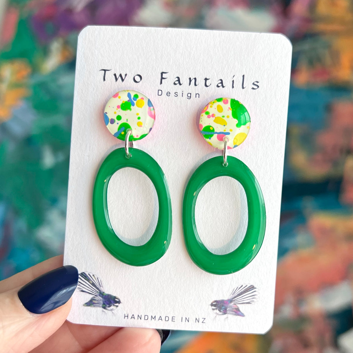 Handmade earrings with cream round studs covered in colourful green yellow pink and blue paint splatters and glossy emerald green oval hoop drops