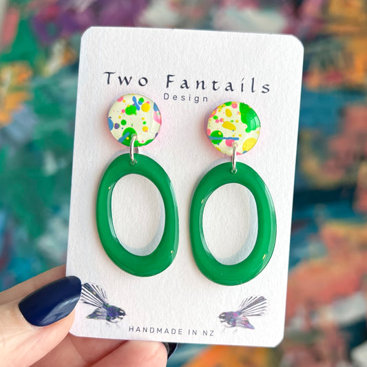 Handmade earrings with cream round studs covered in colourful green yellow pink and blue paint splatters and glossy emerald green oval hoop drops