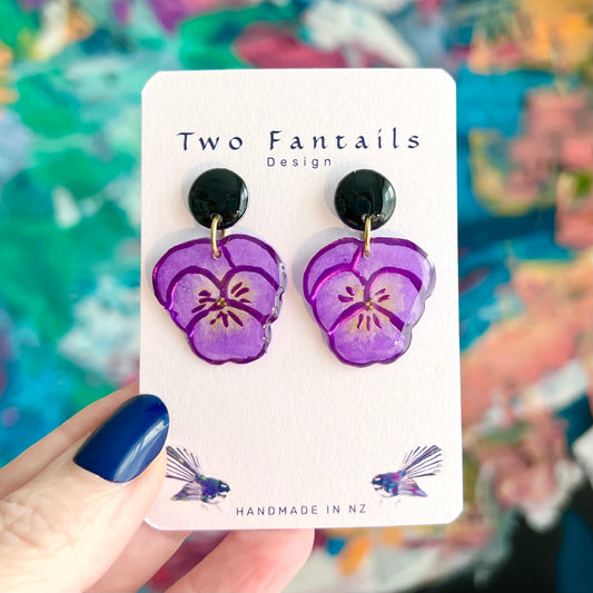 Hand-painted purple pansy flower dangle earrings with glossy black round studs and gold-tone rings by Two Fantails Design