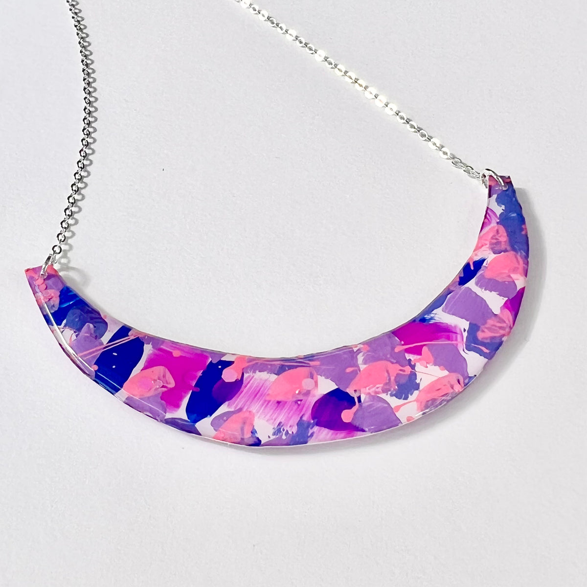 Close-up of hand-painted abstract pink and purple resin-coated crescent pendant