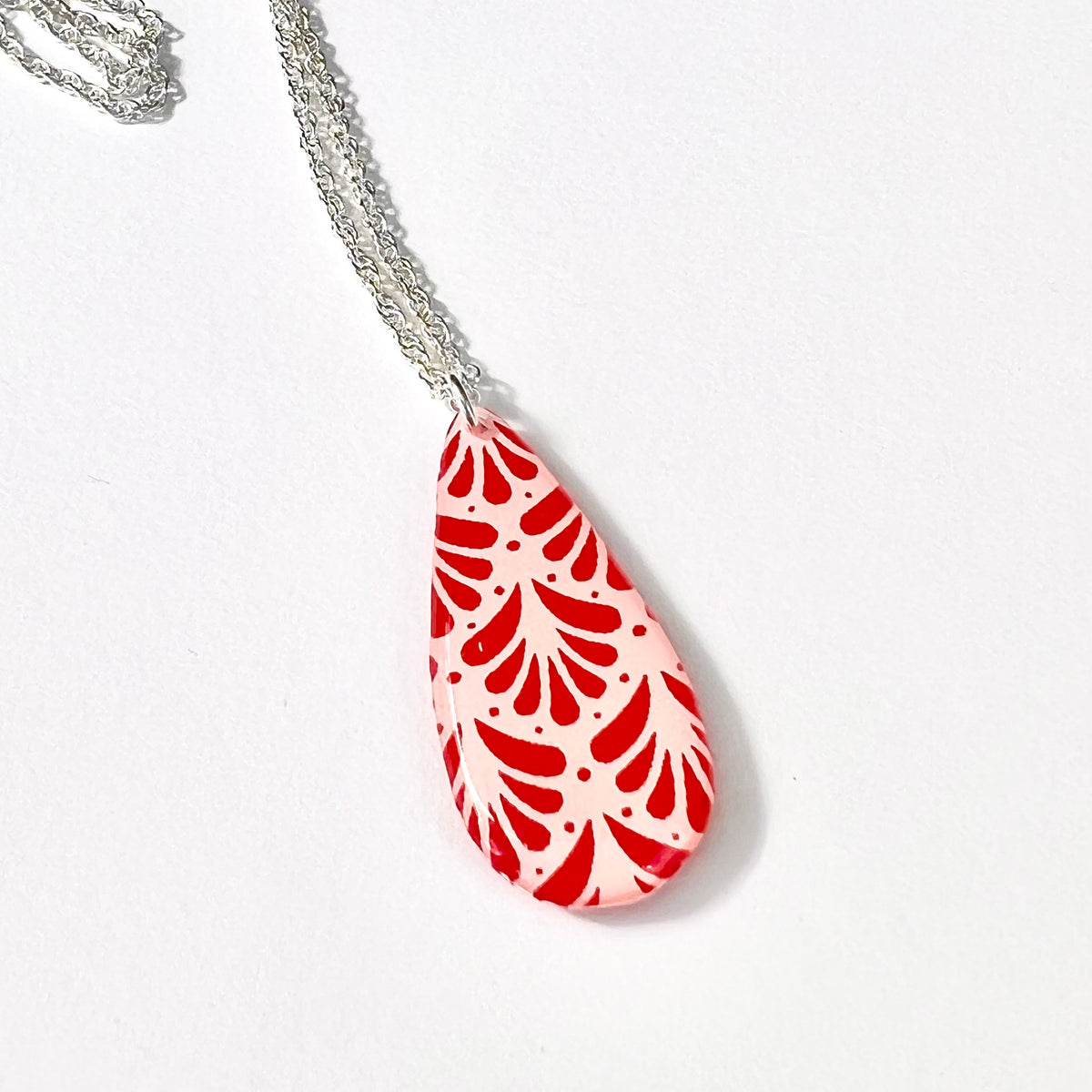 Close-up of red botanical pattern on glossy pale pink teardrop pendant
