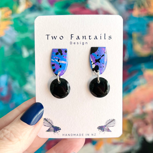 Hand-painted blue, purple and lilac abstract dangle earrings with black paint splatters and glossy black circular drops, by Two Fantails Design.